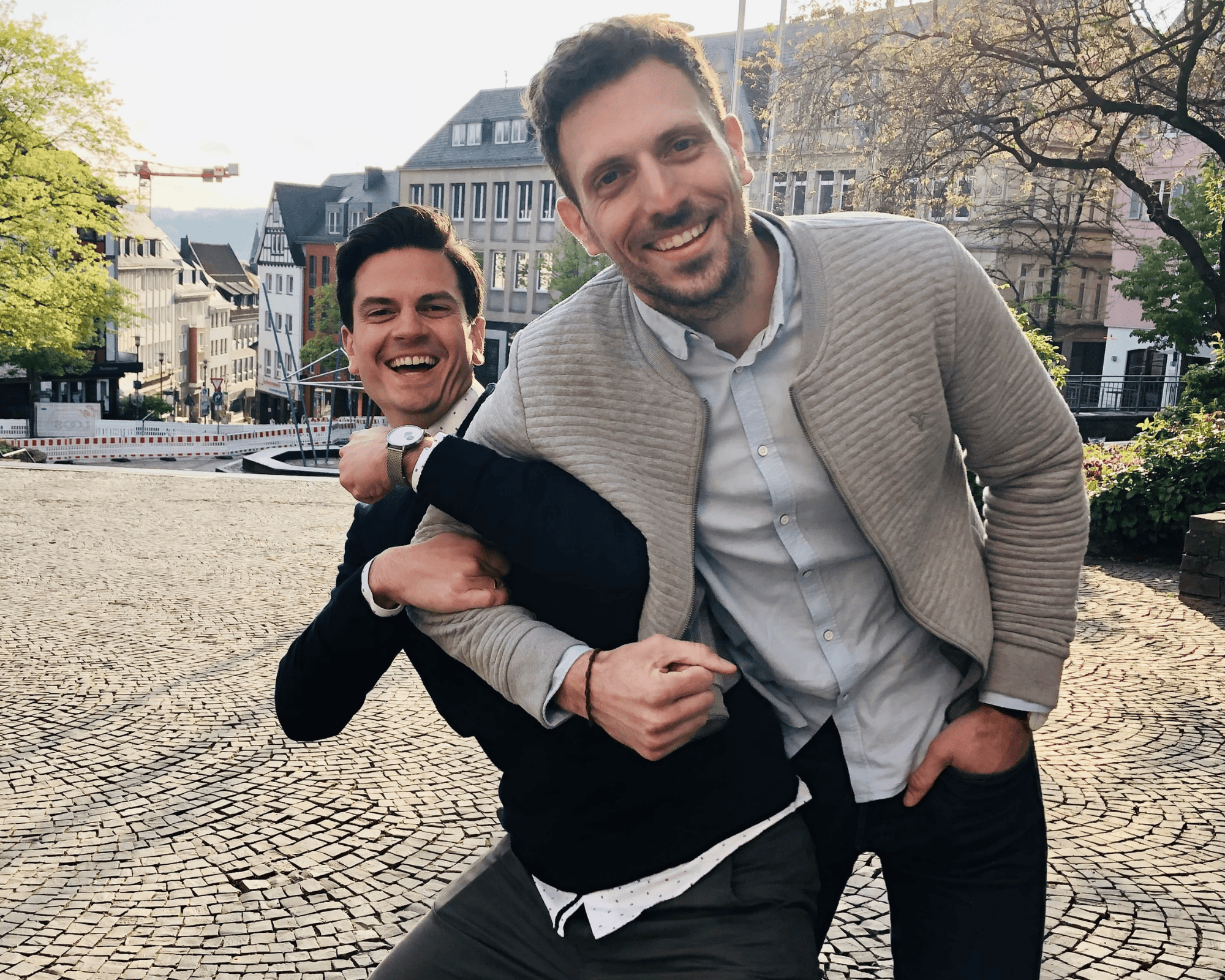 Zwei Gründer stehen lachend nebeneinander auf einem Platz in der Stadt